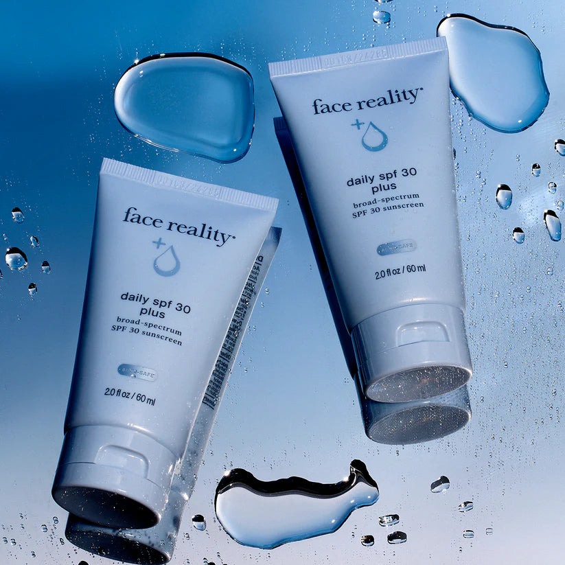 Two bottles of 'face reality' daily SPF 30 Plus sunscreen on a blue background with water droplets.