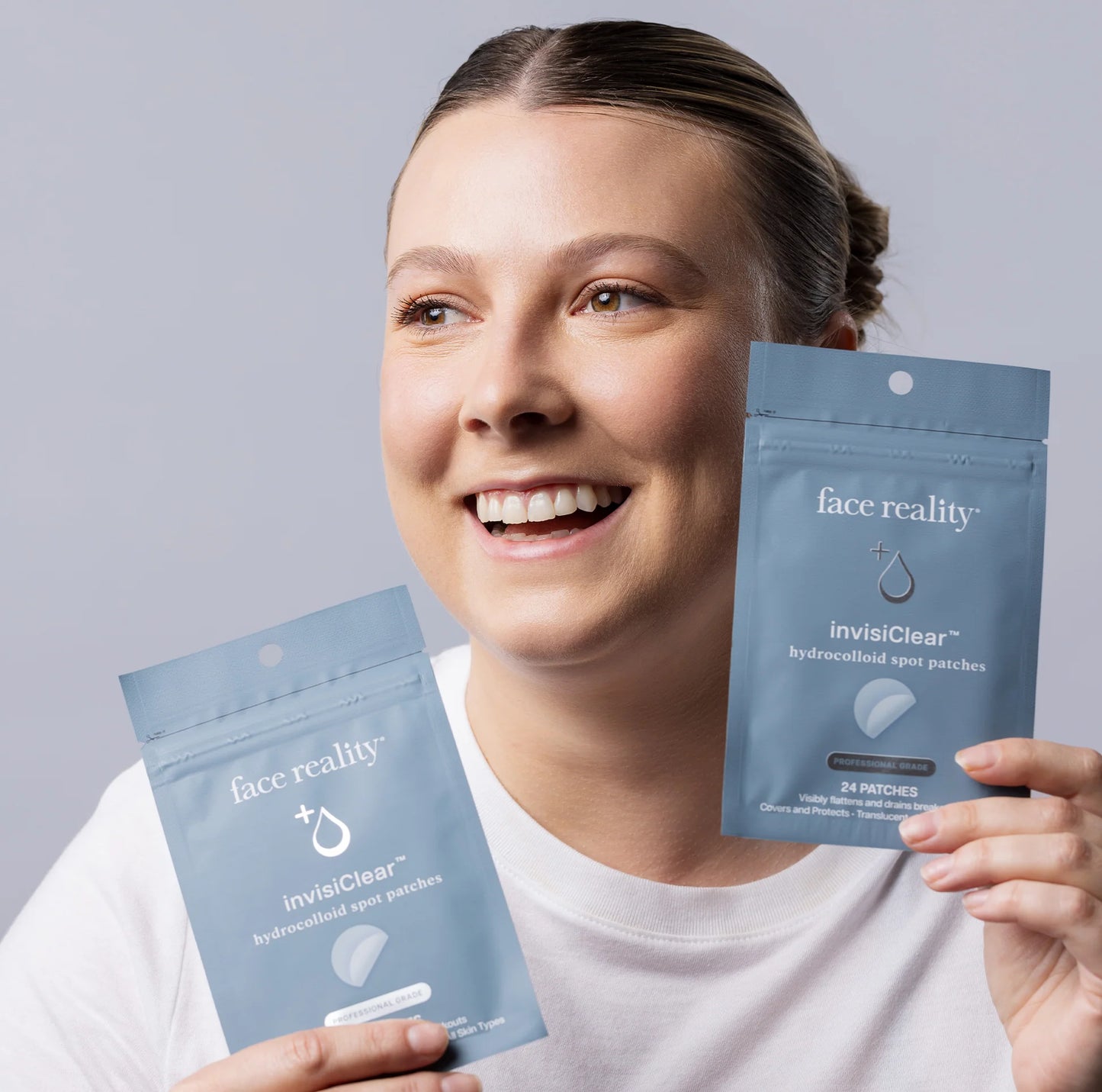 Woman holding two packages of 'face reality' invisClear patches against a gray background